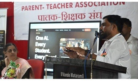 A presenter speaking at the lectern beside a presentation display